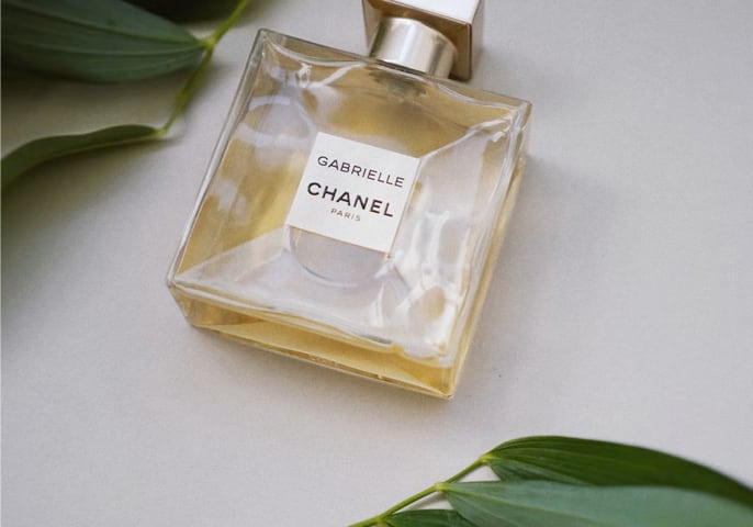 Gabrielle Essence parfum bottle laying flat on a table width green leaves above and below it.